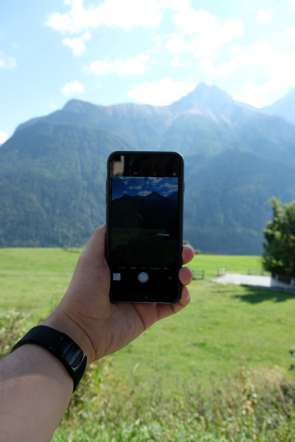 Das Bild zeigt den Blick durch das Handy auf die Berge